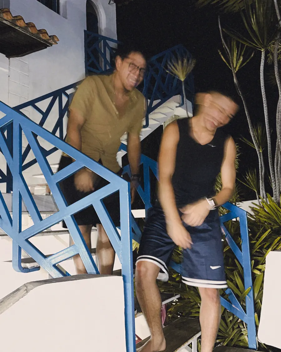 Dos amigos bajan unas escaleras de baranda azul de noche en Higuerote.
