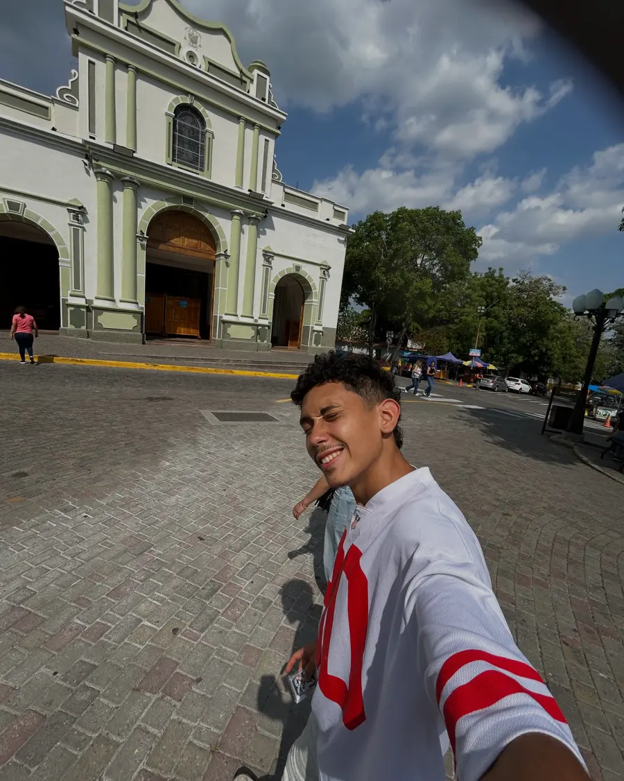 Dani sonríe con su camiseta 90 frente a una iglesia blanca y verde.