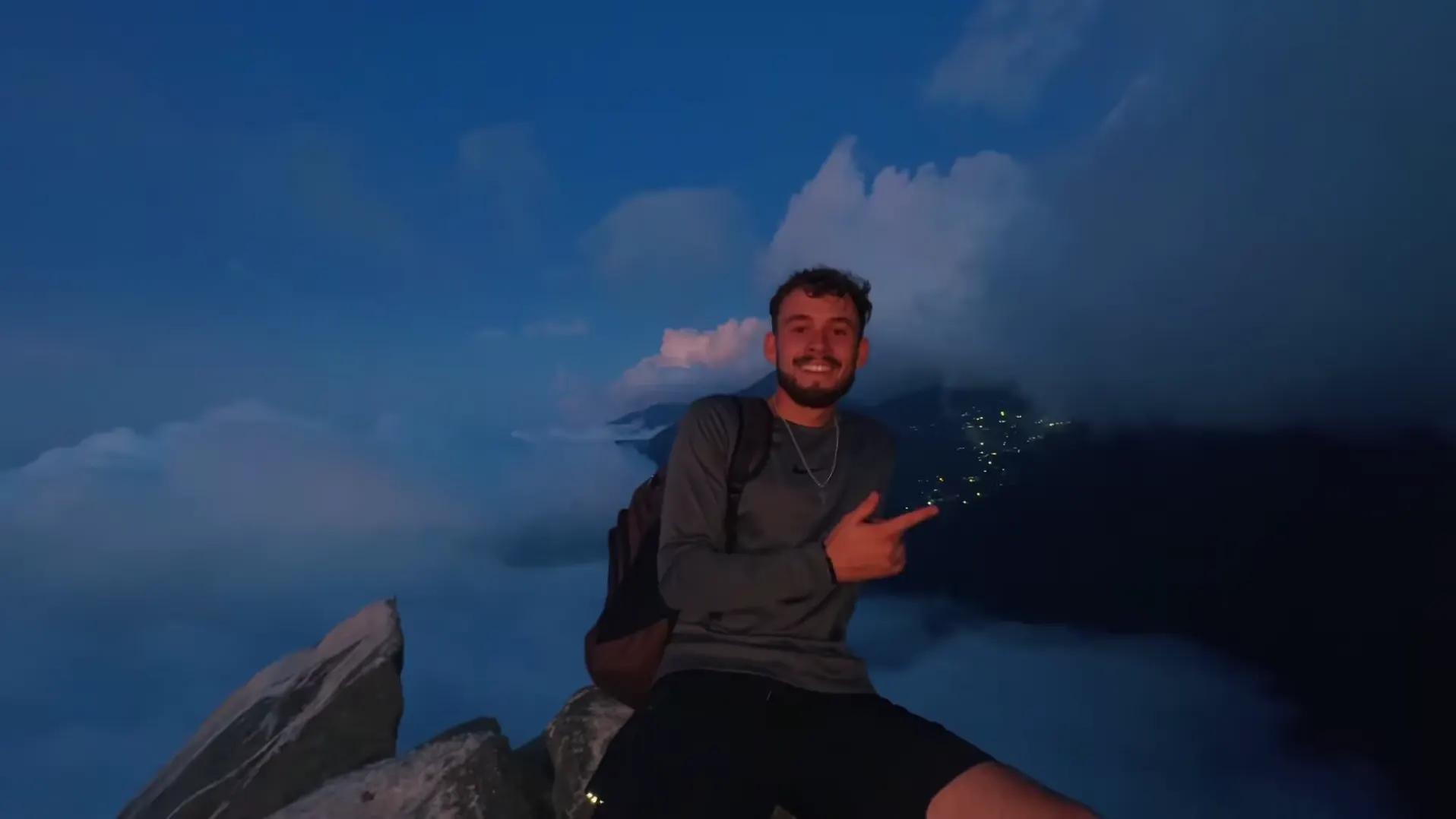 Galipán: un creador sentado en una roca de noche, con nubes y luces abajo.